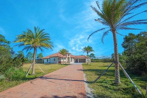 Uma casa de dois andares com telhado de telhas vermelhas, uma garagem e um caminho de paralelepípedos até a entrada.