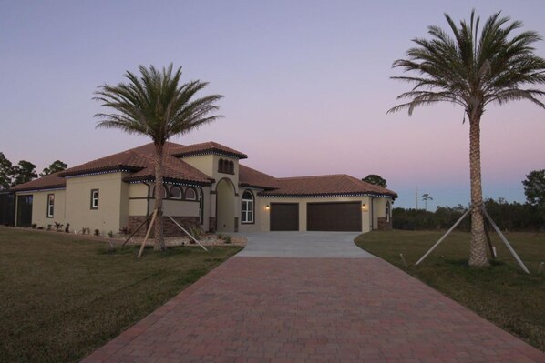 A two-story house with a tiled roof, a garage, and a paved driveway. - Stunning Luxury Mediterranean-style Private Oasis! (Grant-Valkaria)