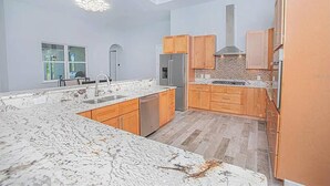 Une cuisine moderne dotée de plans de travail en granit, d’armoires en bois et d’un réfrigérateur en acier inoxydable.