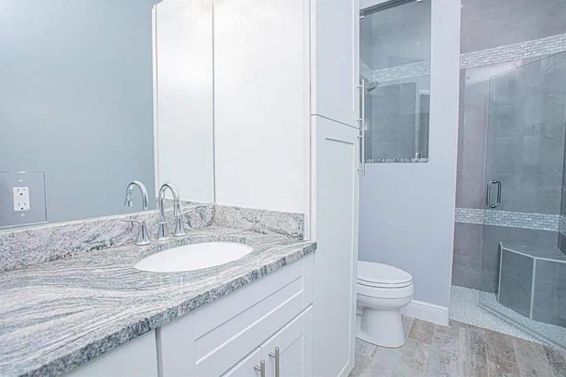 Un baño con lavamanos de encimera de granito, inodoro y ducha con mampara de cristal.