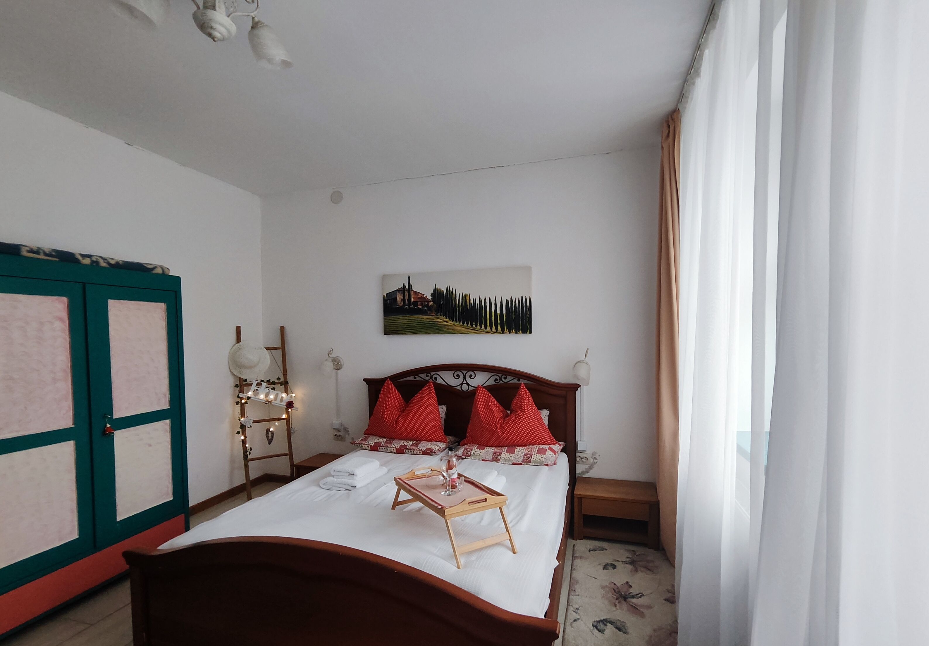 A neatly made bed with a tray, red pillows, and a painting on the wall.