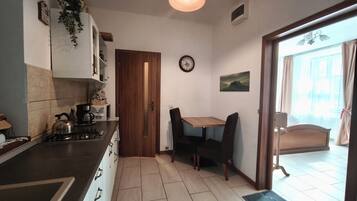 A kitchen with a wooden door, a dining table with chairs, a clock on the wall, and a view through a window.