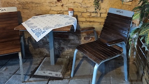 Een terras met een tafel en twee stoelen, een 'WELCOME' bord en een 'SUS' bord aan de muur.