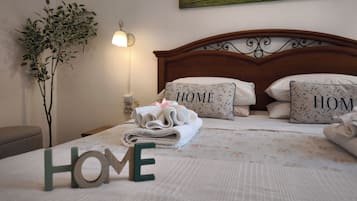 A neatly made bed with 'HOME' pillows and a 'HOME' sign, a wall-mounted painting, a bedside lamp, and a potted plant.