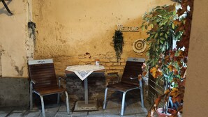 Un petit espace extérieur aménagé avec deux chaises en bois et une table, une pancarte indiquant « BIENVENUE » et une plante en pot.