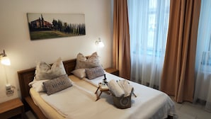 Un lit bien fait, avec des oreillers sur lesquels est écrit le mot « MAISON », une table de chevet avec une lampe et un tableau accroché au mur.