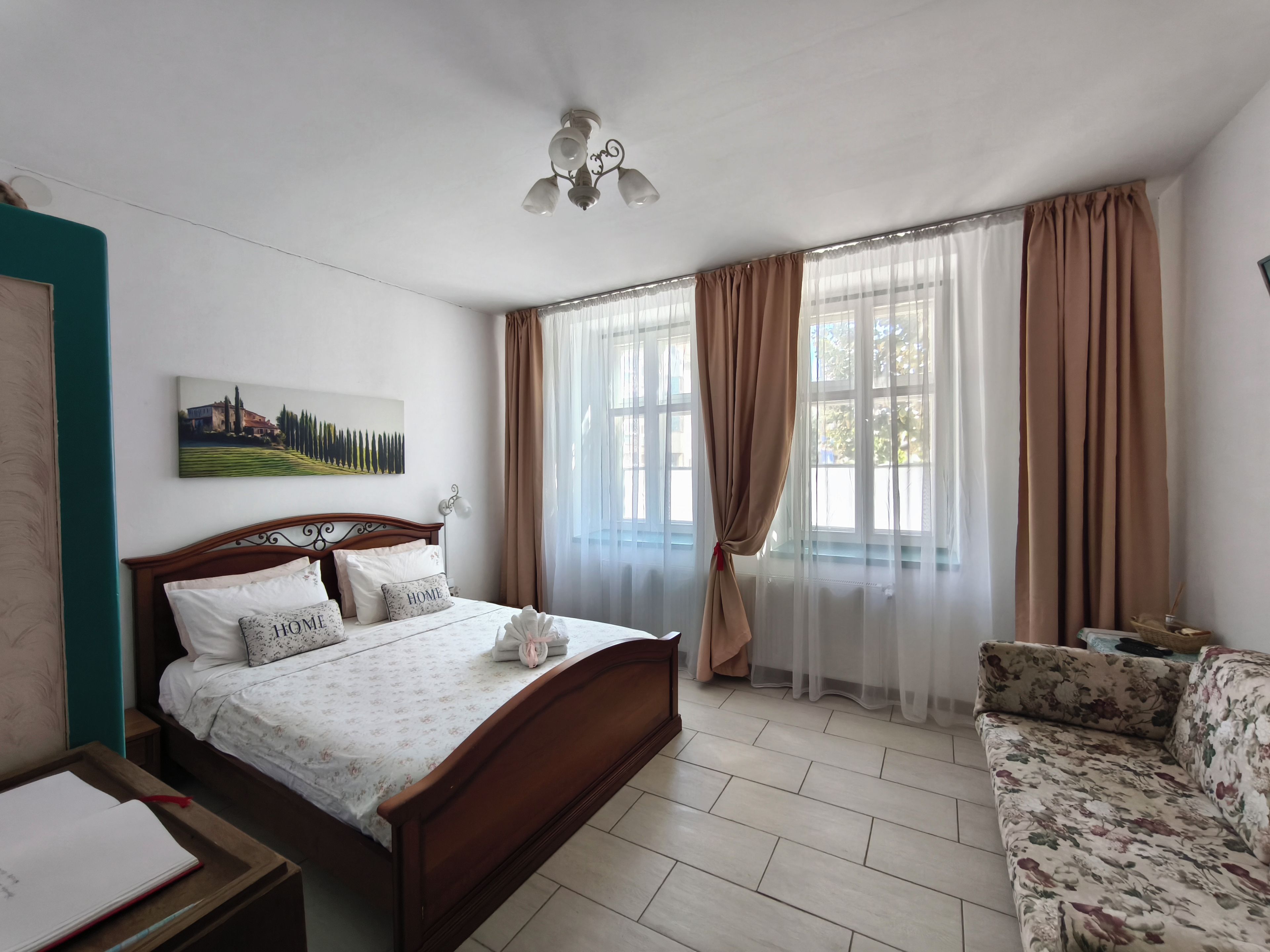 A bedroom with a wooden bed, a sofa, a painting on the wall, and a ceiling fan.