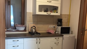 Een kleine keuken met witte kastjes, een waterkoker, een magnetron en een koffiezetapparaat.