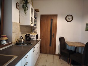 A compact kitchen with a wooden door, a clock, and a dining area with a table and chairs. - Buon Studio Sibiu, near train station and Small Square Old Town (Sibiu)