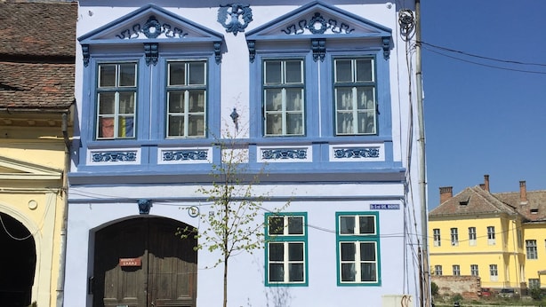 Un bâtiment à deux étages avec une entrée centrale et un petit arbre devant.