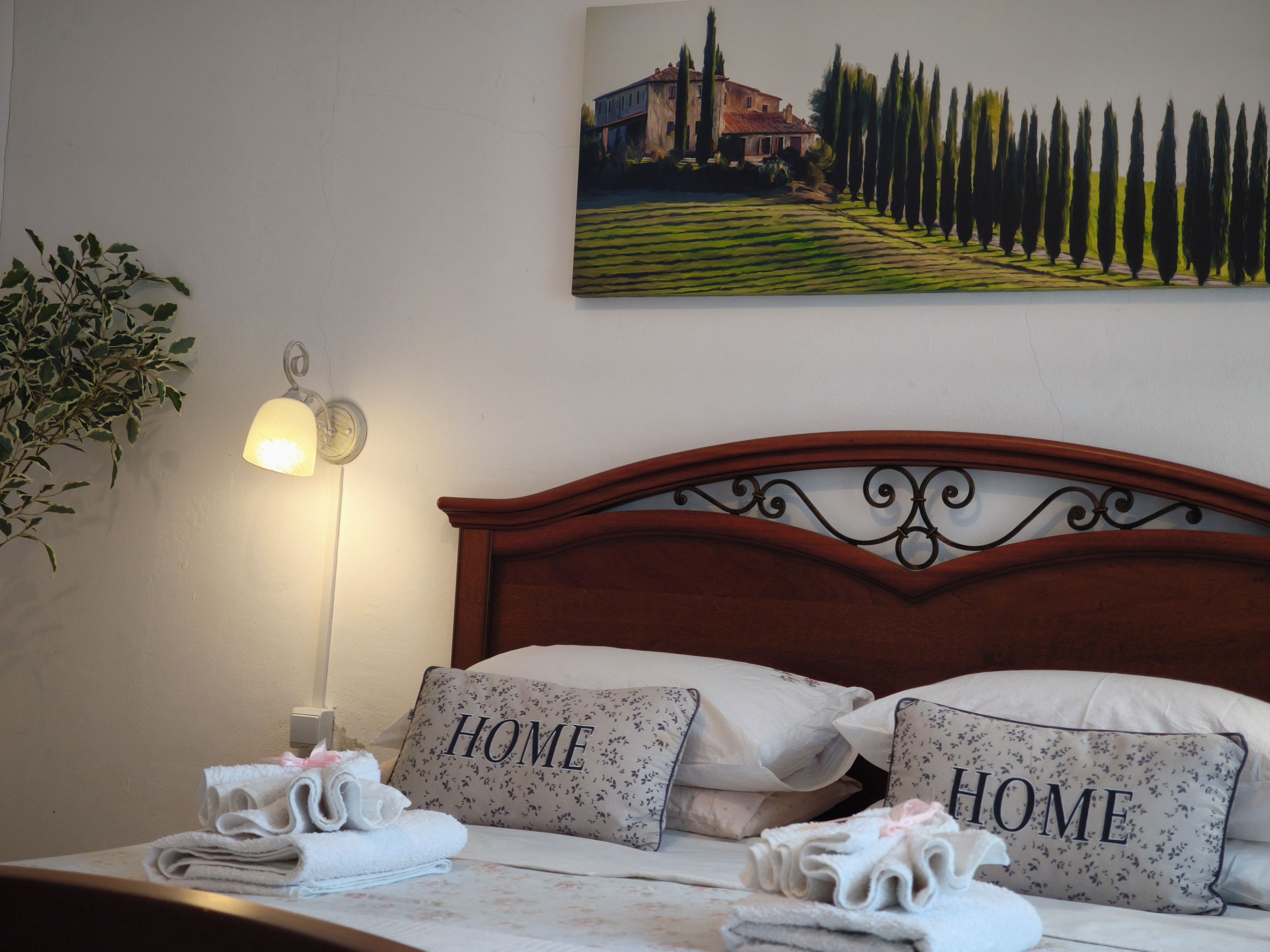 A neatly made bed with pillows labeled 'HOME' and a painting of a landscape on the wall.