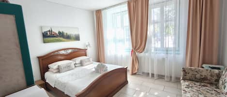 A bedroom with a wooden bed, a nightstand, a floral sofa, and a window with sheer curtains.