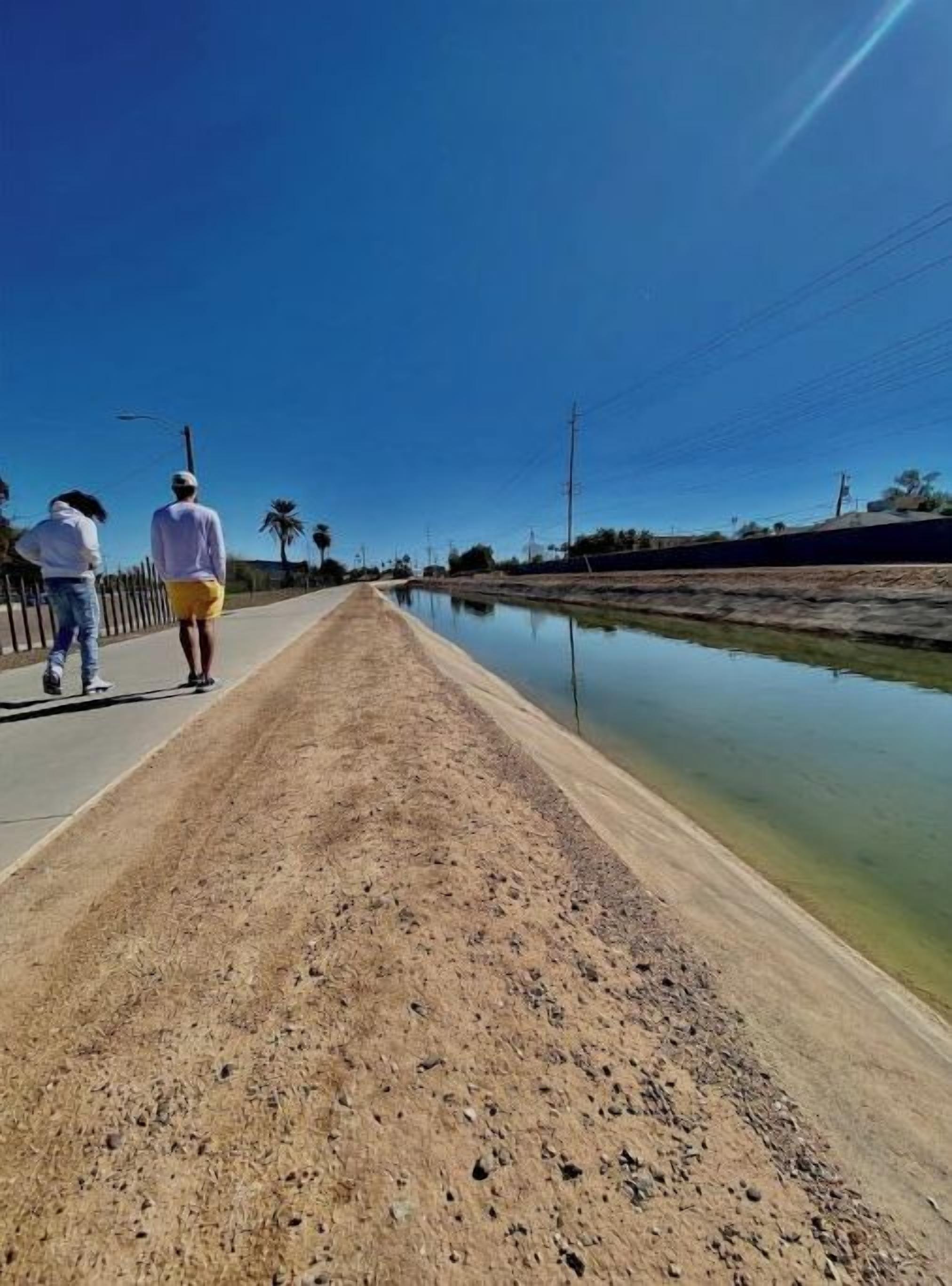 Un sendero al lado de una masa de agua tranquila, con cielo despejado arriba.