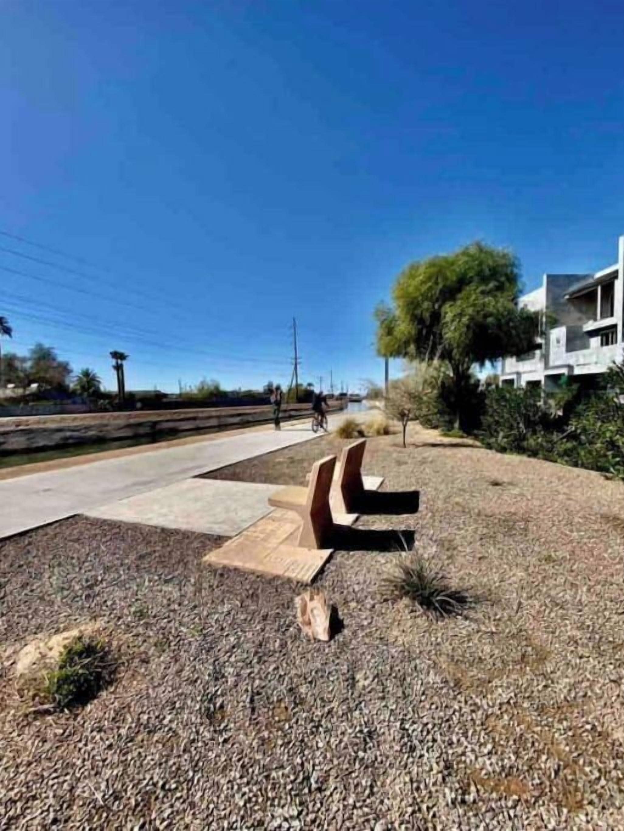 A paved walkway with benches, a clear sky, and a building with a modern design in the background.
