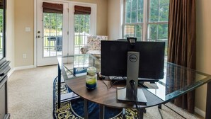 Um escritório em casa com uma mesa de vidro, um computador Dell e vista para uma varanda e área externa.