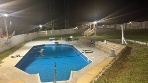 Piscina retangular com escada de metal, cercada por um deck de concreto.
