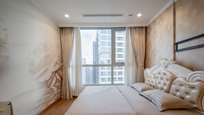 Een moderne slaapkamer met een groot bed, uitzicht op hoge gebouwen en een plafond met inbouwverlichting.