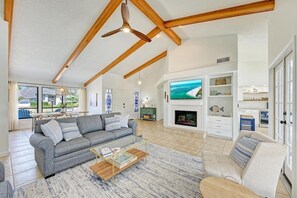A spacious living room with a high ceiling, a fireplace, a television, and a view of the outdoors.