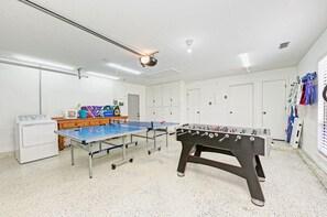 A room with a foosball table, ping pong table, and a washing machine.