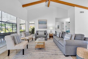 A spacious living room with a high ceiling, a sofa set, a coffee table, and a painting on the wall.