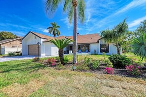 A residential property with a garage, a covered patio, and a well-maintained lawn with various plants and a palm tree.