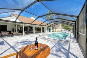 A covered outdoor area with a pool, wooden table, and chairs.