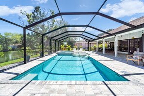 Piscina coberta com vista para um lago e árvores, rodeada por um espaço de varanda com mobiliário de exterior.