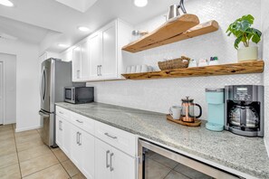 Una cocina moderna con armarios blancos, un refrigerador de acero inoxidable, un microondas, una cafetera y estantes de madera con utensilios de cocina.