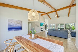 A spacious living area with a wooden dining table, a large sofa set, and a view of the outdoors through large windows.