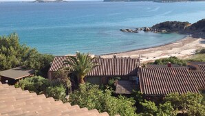 Vista costera con edificios de tejados de terracota, una playa de arena y un faro a lo lejos.