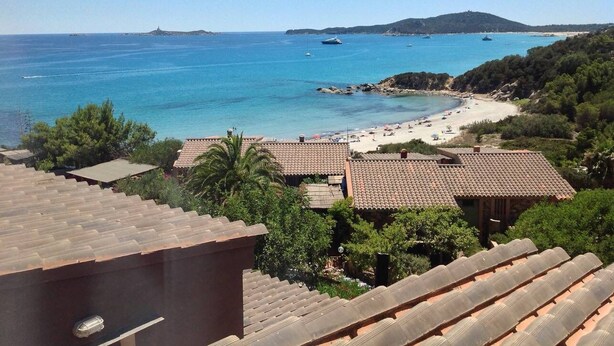 Vista costera con playa, mar azul cristalino y un paisaje montañoso en la distancia.