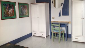 Una habitación con un armario blanco, un escritorio con silla y dos cuadros abstractos en la pared.