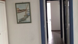 Un pasillo con suelo de baldosas, un marco de puerta y un cuadro de un velero en la pared.