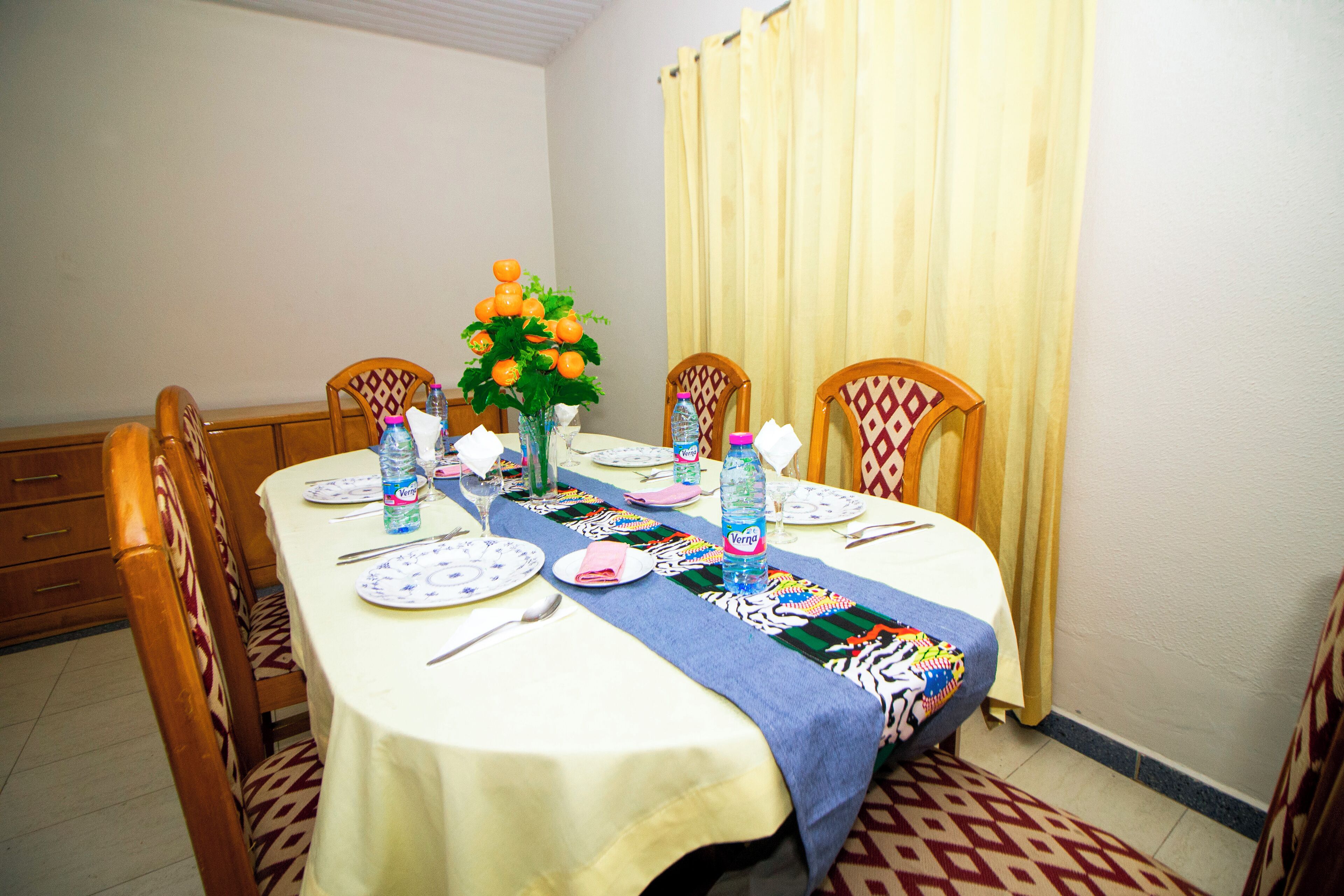 A dining table set for four with a tablecloth, placemats, plates, cutlery, and a water bottle.