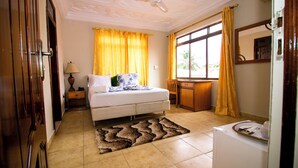 Un dormitorio con cama, escritorio, silla, ventana con cortinas, ventilador de techo y radiador.