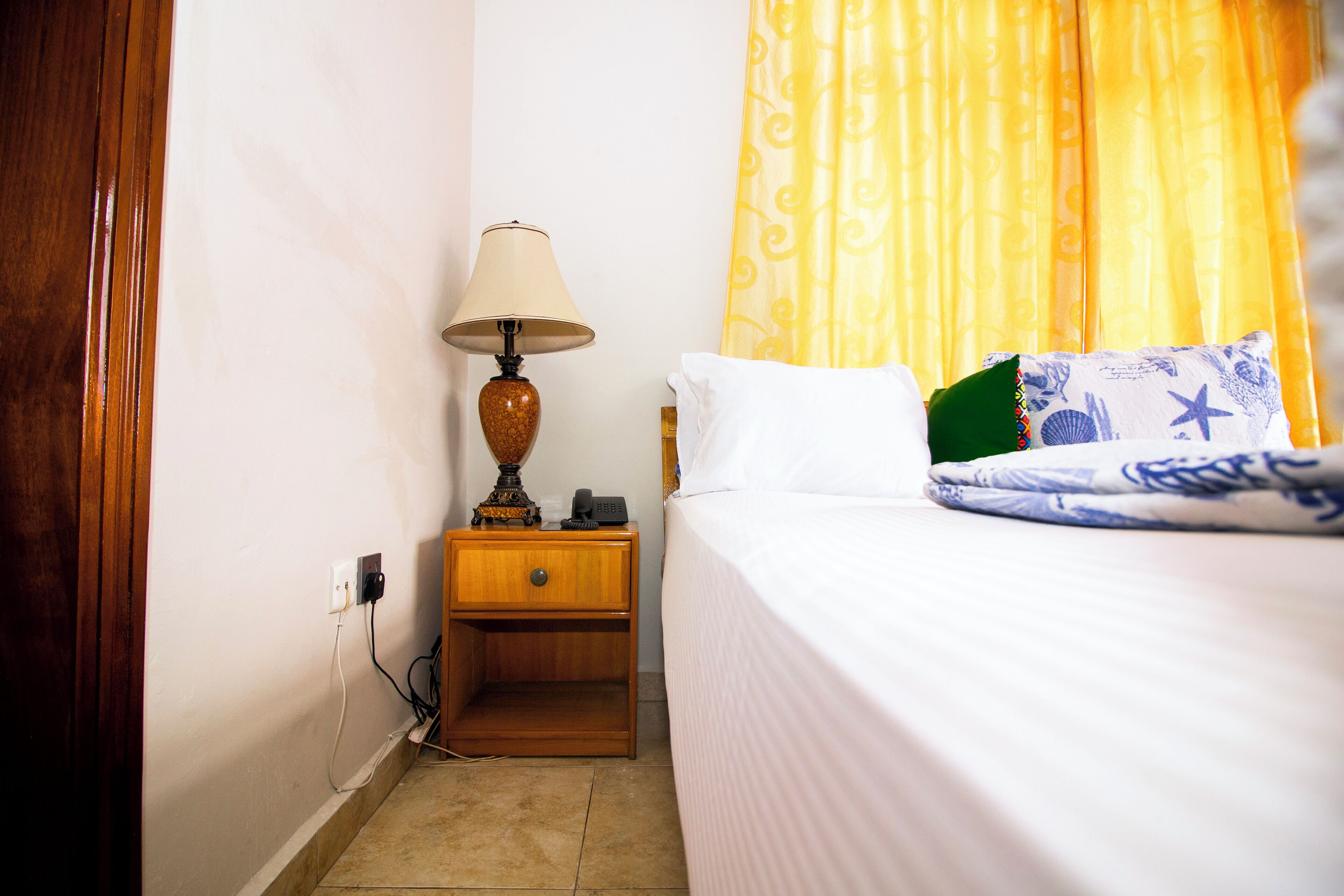 A hotel room with a bed, a nightstand with a lamp, and a curtain.
