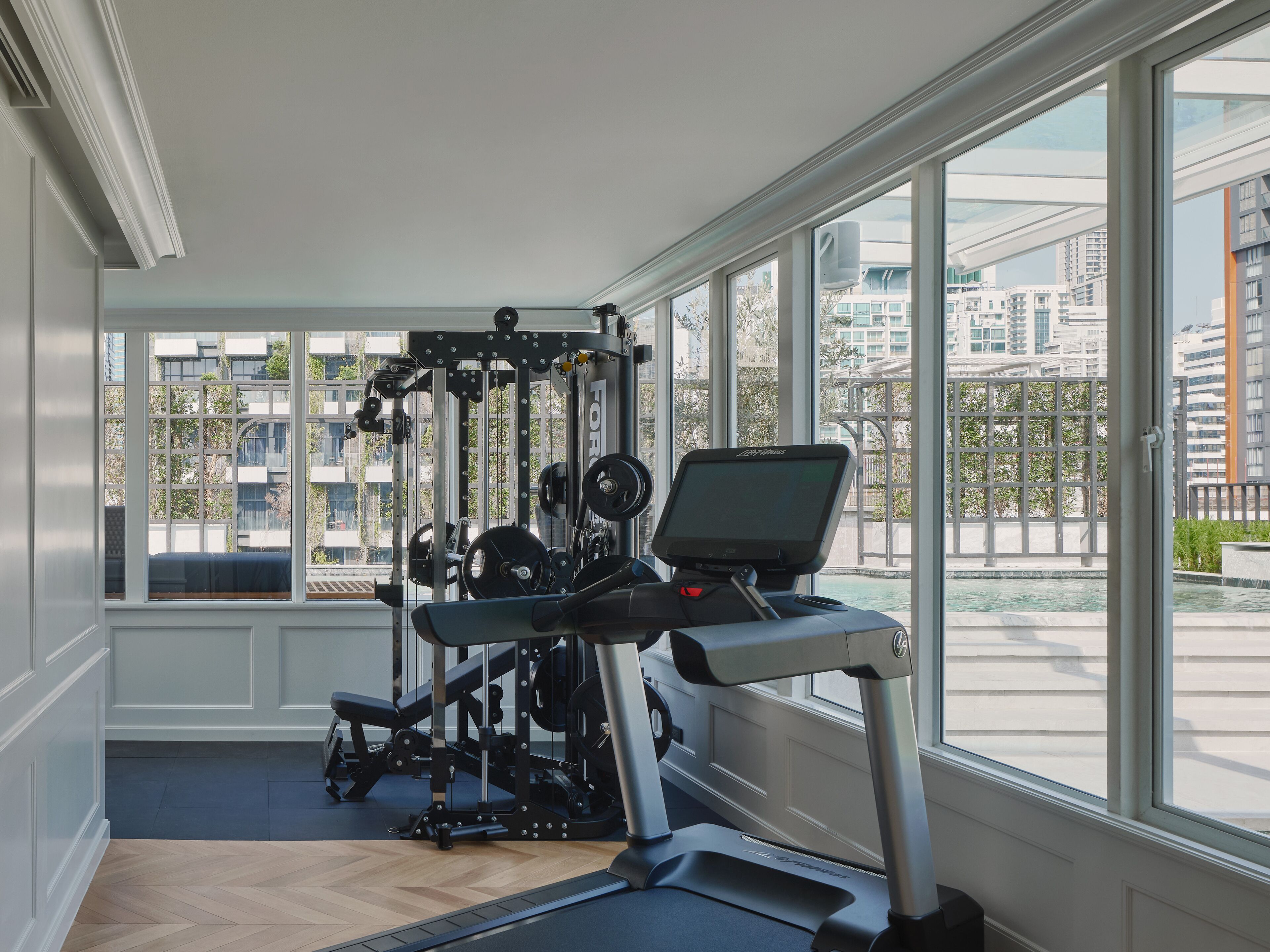Ein Fitnessstudio mit Trainingsgeräten und großen Fenstern mit Blick auf eine Stadtlandschaft.