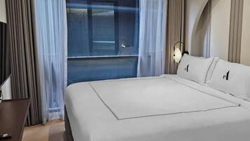 A hotel room with a bed, a TV, a desk, and a window with curtains.