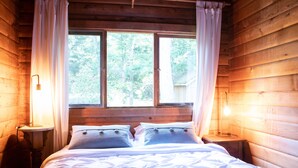 Een slaapkamer in een houten chalet met een bed, twee bedlampen en een raam met gordijnen.