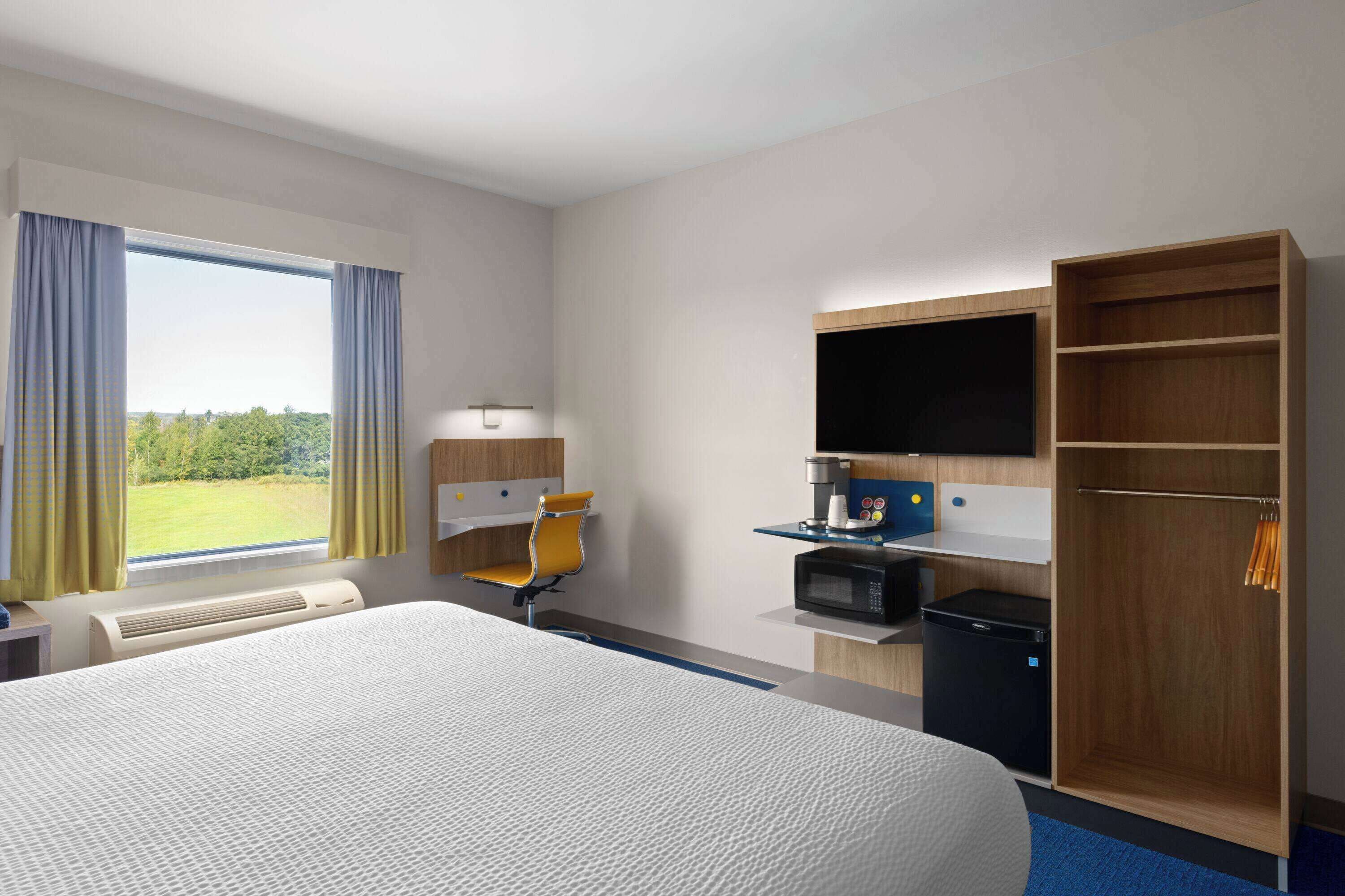 A hotel room with a large bed, a desk with a chair, a microwave, a wardrobe, and a TV.