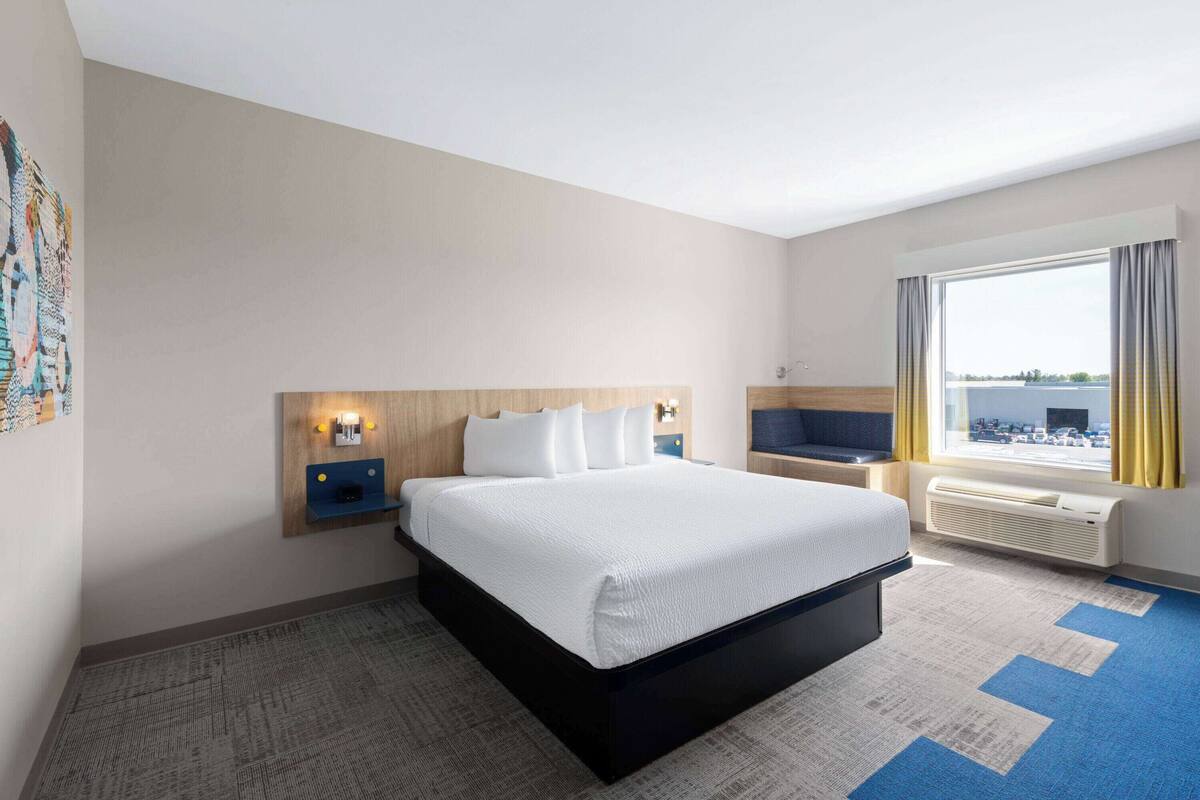 A hotel room with a large bed, a desk with a chair, a window with curtains, and a wall-mounted TV.