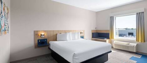 Une chambre d’hôtel avec un grand lit, un bureau avec une chaise, une fenêtre avec des rideaux et un téléviseur fixé au mur.