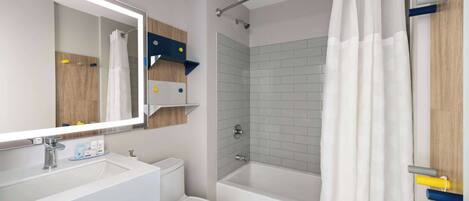 A modern bathroom with a white sink, toilet, and bathtub. There is a mirror above the sink, and a shower curtain is visible.