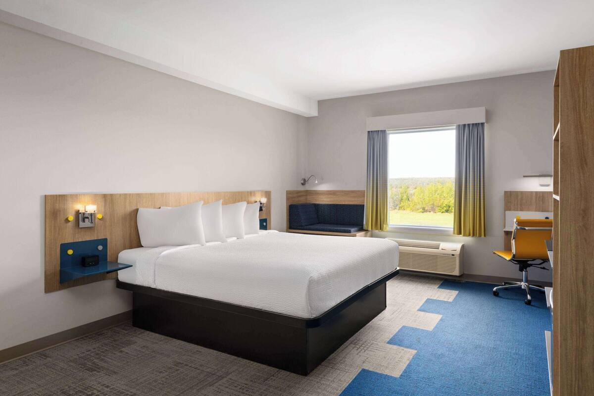 A hotel room with a large bed, a desk, a chair, a TV, and a window with curtains.