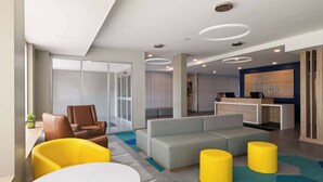 A modern lobby with a sofa, chairs, a reception desk, and a patterned carpet.