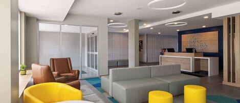 A modern lobby with a sofa, chairs, a reception desk, and a patterned carpet.