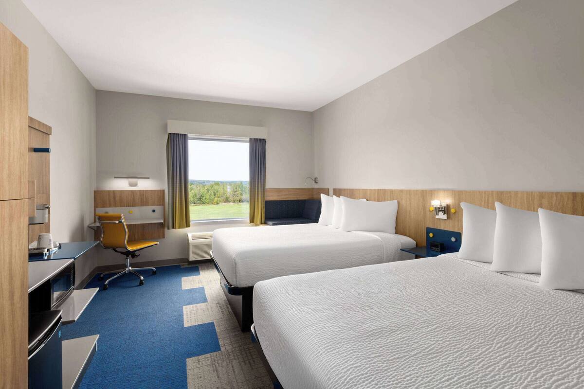 A hotel room with two beds, a desk, a chair, and a window with a view.