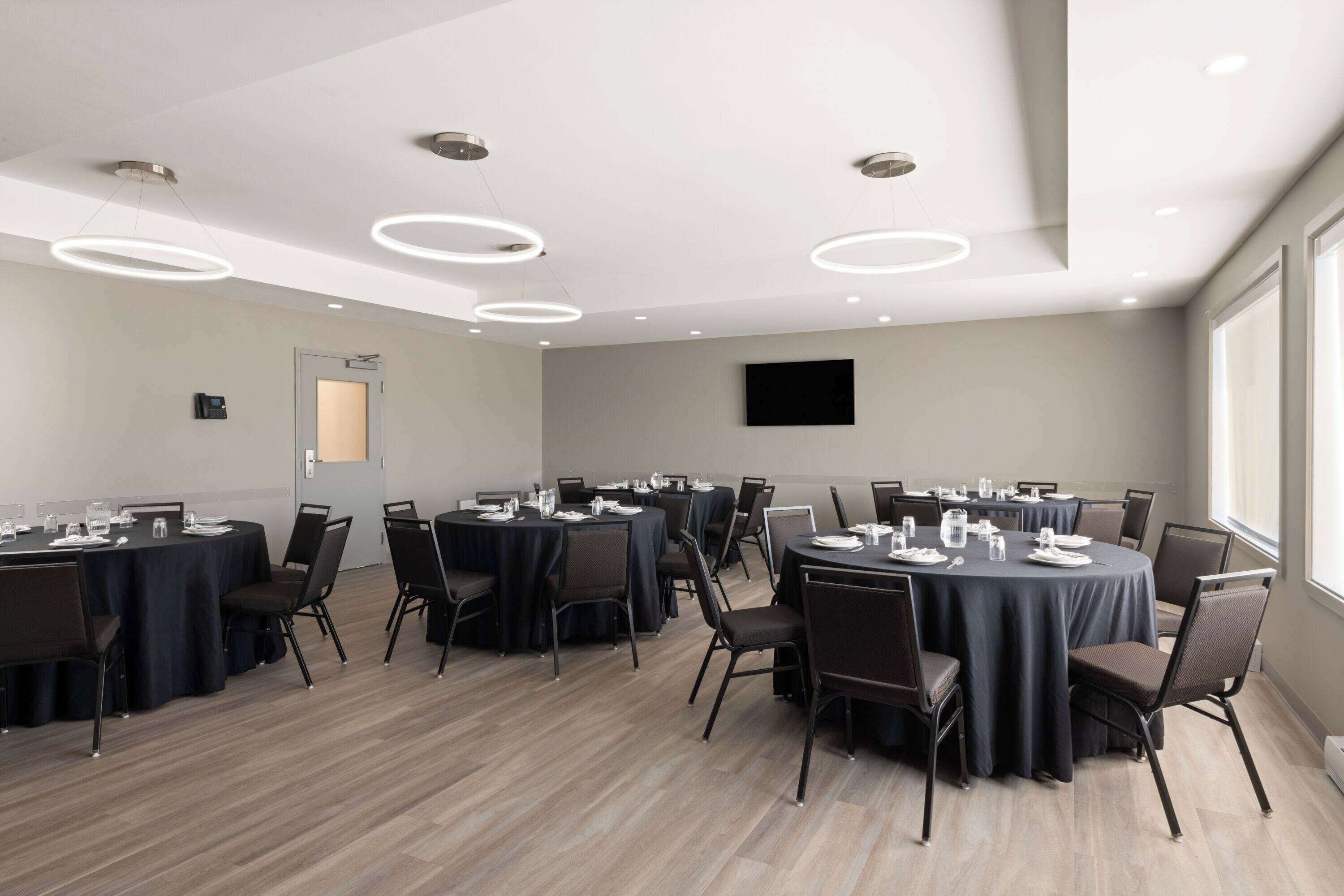 A conference room with round tables, chairs, and a flat-screen TV on the wall.