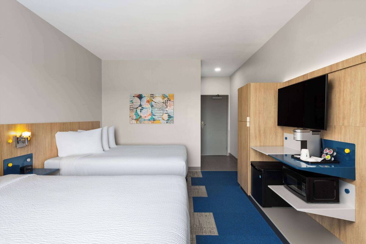 A hotel room with a bed, a desk with a flat-screen TV, a microwave, and a small kitchenette.