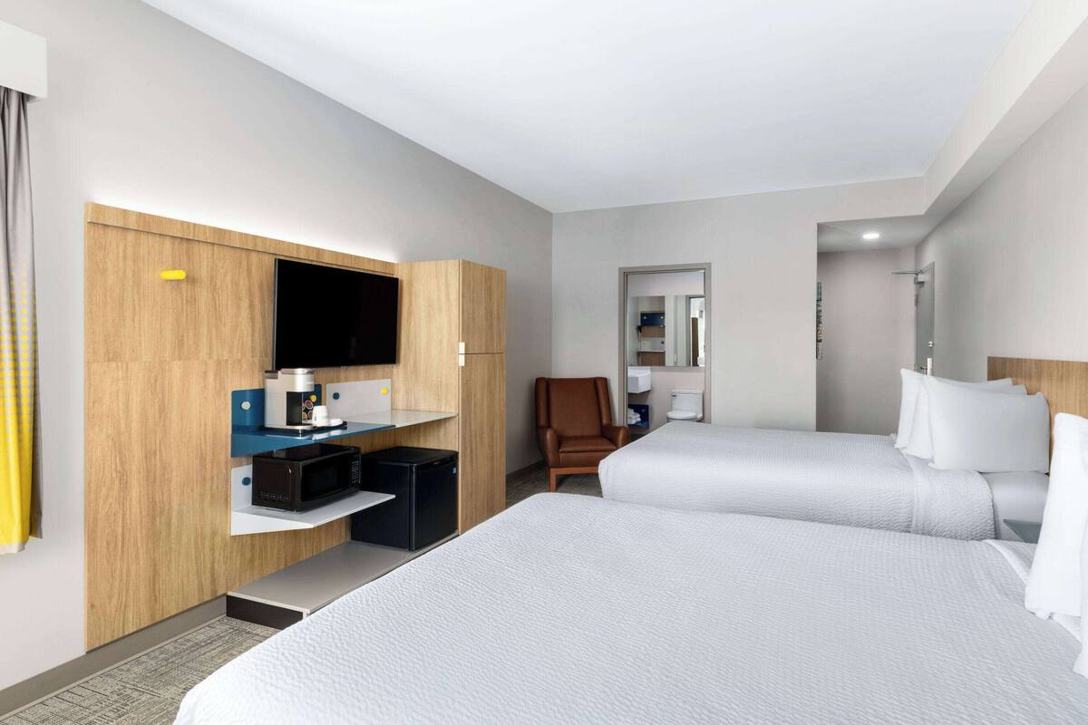 A hotel room with two beds, a desk with a microwave, a chair, and a TV.